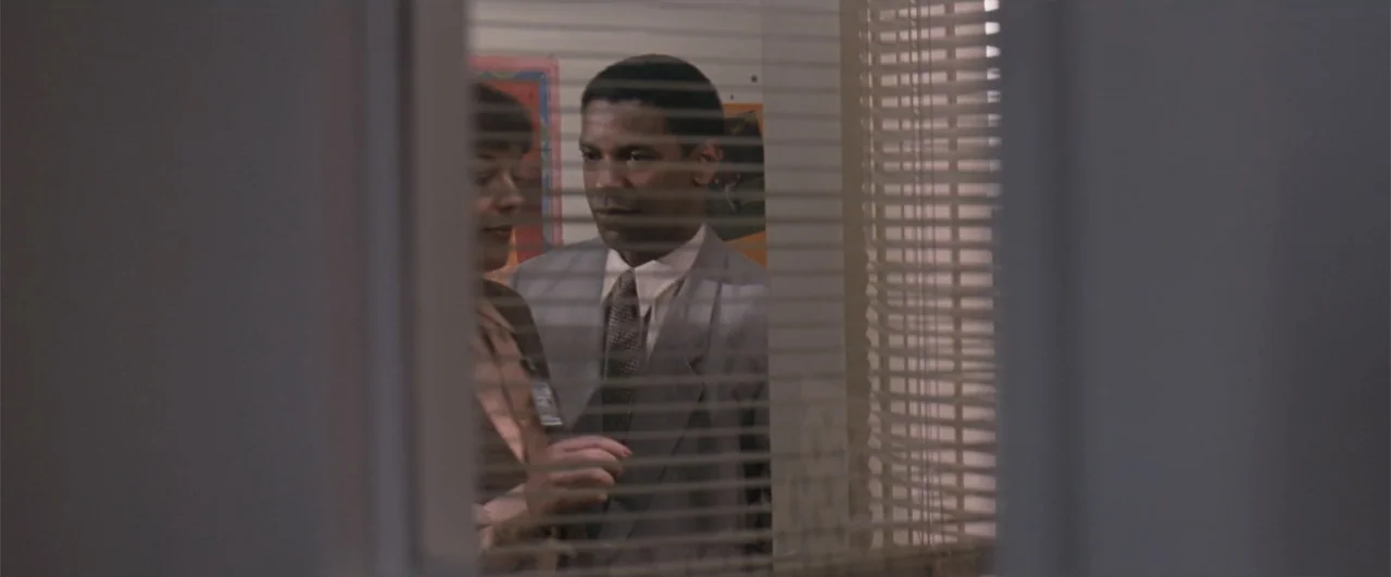 The Pelican Brief (1993) movie still: medium — A professional interior office space features a man and woman seen through venetian blinds. They…
