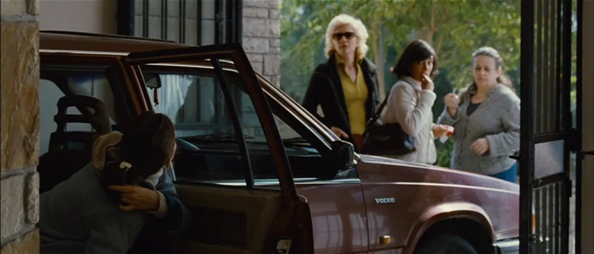 The Headless Woman (2008) movie still: medium — A brown Volvo station wagon is parked in a driveway near a stone wall. Three women stand outside the…