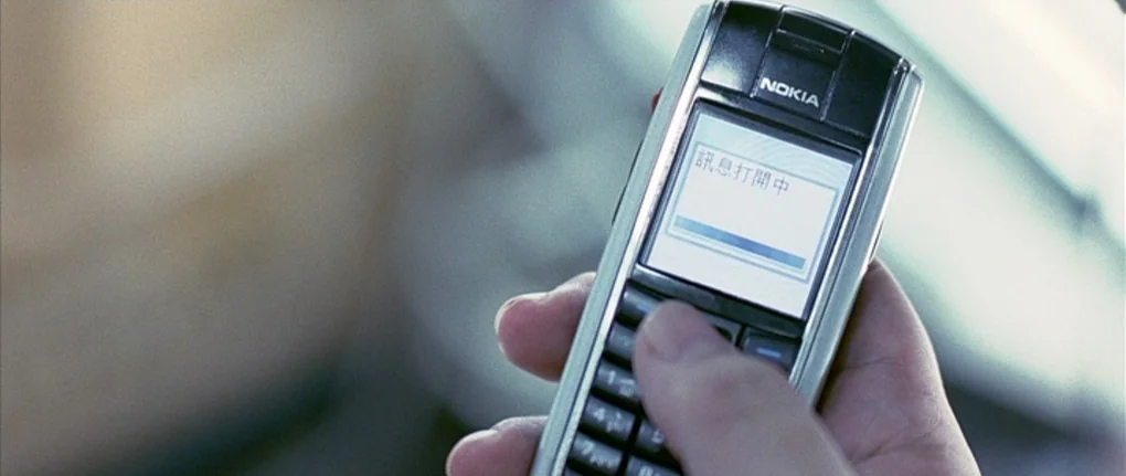 Boarding Gate (2007) movie still: closeup — A close-up of a silver-and-black Nokia candy-bar mobile phone held in a hand. The screen shows a…