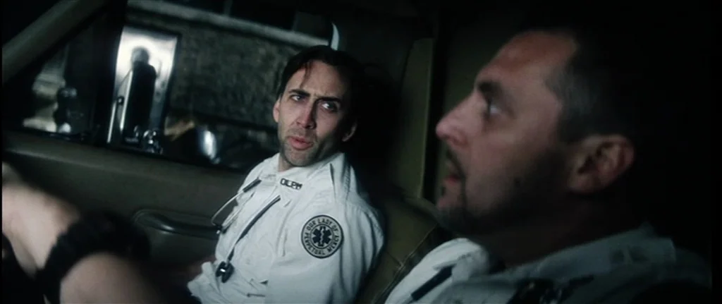 Bringing Out The Dead (1999) movie still: medium — The front cabin of an ambulance at night with dimly lit control panels. Two paramedics in white…
