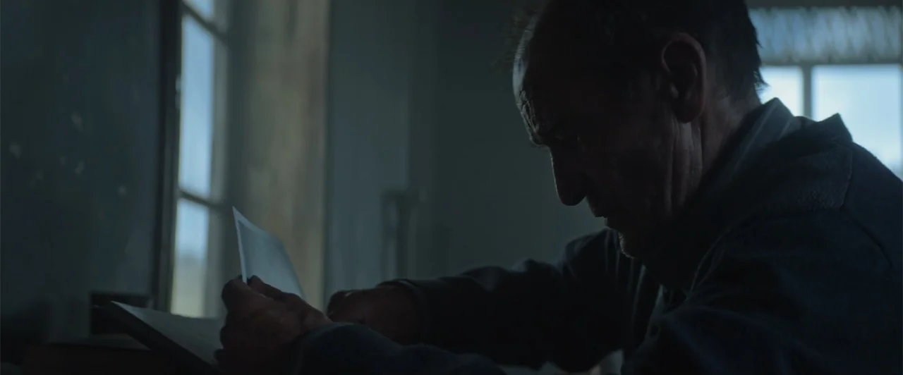 My Neighbor Adolf (2022) movie still: medium — A dimly lit room features a window with daylight filtering through the panes. An elderly man with…