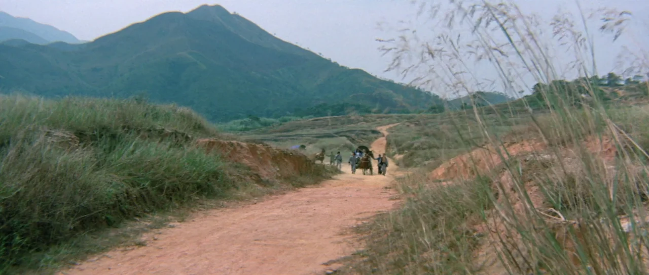 The Legend of the 7 Golden Vampires (1974) movie still: wide — A wide, dry, dirt road winds through an open valley toward a large green mountain. A…