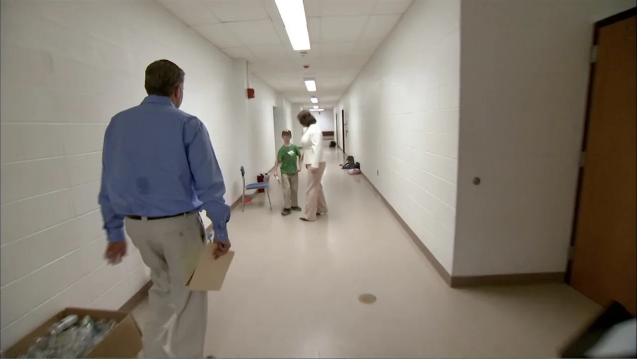 Life According to Sam (2013) movie still: medium — A long institutional corridor features white block walls and a linoleum floor. A man in a blue…