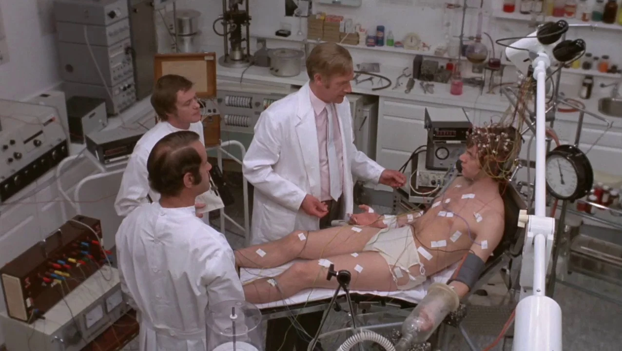 O Lucky Man! (1973) movie still: wide — A stark, sterile medical laboratory filled with electronic monitoring equipment and wires. Three men in lab…