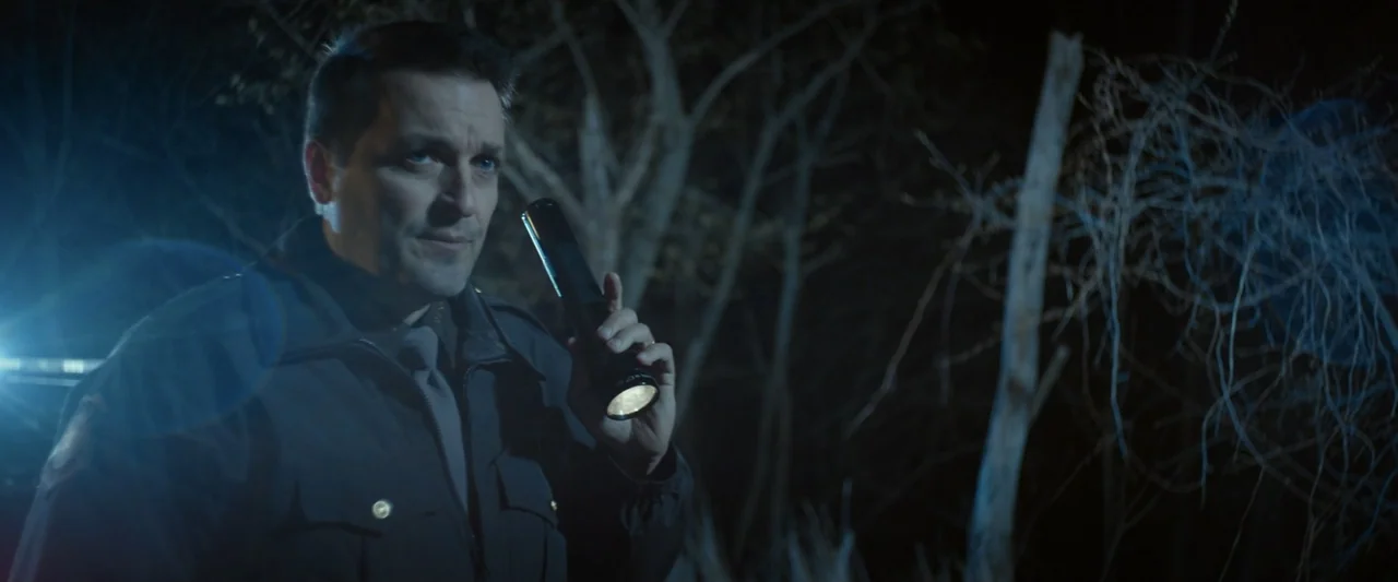 God Bless the Broken Road (2018) movie still: medium — A dark, dense woodland setting at night with bare tree branches and sparse brush. A uniformed…
