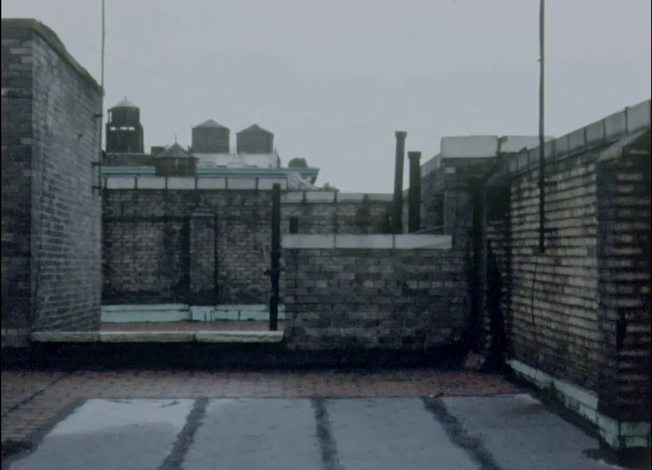 Hotel Monterey (1973) movie still: establishing — A flat urban rooftop features aged brick parapets and weathered black tar roofing material.…