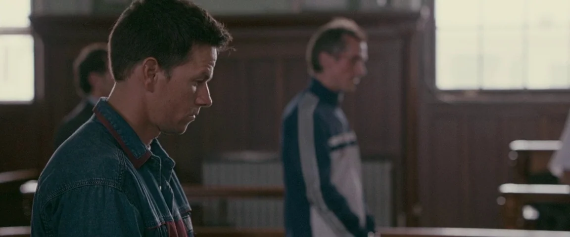 The Fighter (2010) movie still: medium — A courtroom interior with wood paneling and rows of benches for attendees. Two men sit in profile facing…