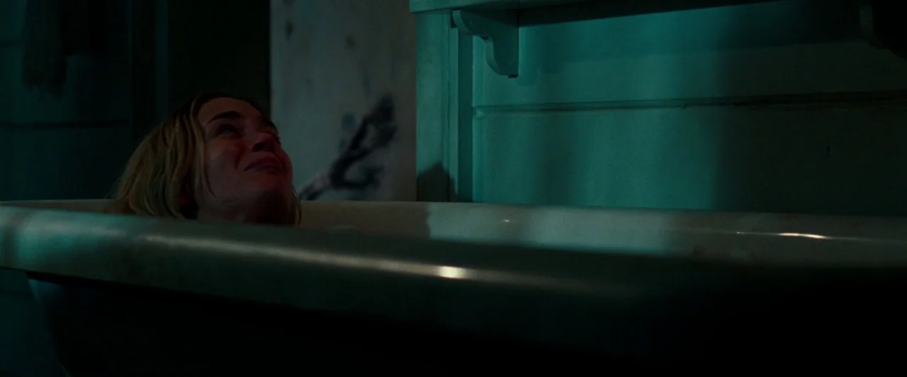 A Quiet Place (2018) movie still: medium — A dimly lit room with a vintage bathtub against a teal painted wall. A woman lies submerged in the tub,…