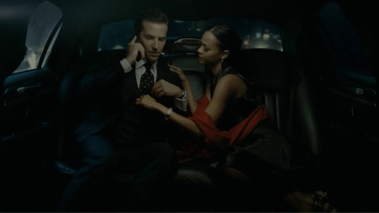 The Words (2012) movie still: medium — The interior of a moving vehicle at night with blurred city lights visible through glass. A man in a dark…