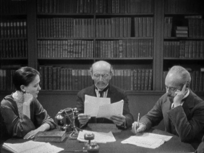 The Last Command (1928) movie still: medium — A quiet room features a large table positioned in front of floor-to-ceiling bookshelves. A woman and…