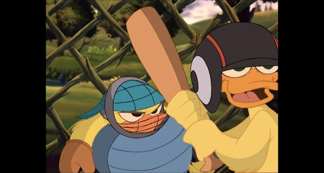 The Sissy Duckling (1999) movie still: medium — Two cartoon ducks stand near a chain link fence on a grass field. One duck holds a wooden baseball…