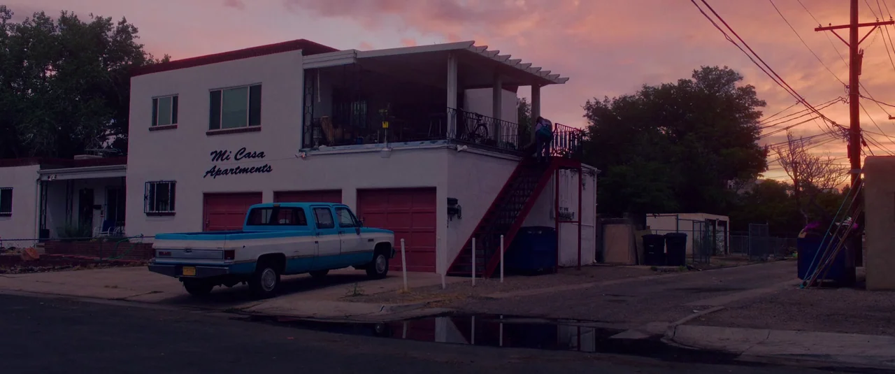Love Lies Bleeding (2024) movie still: wide — A low-rise residential building with red garage doors and a staircase leading upstairs. A vintage blue…