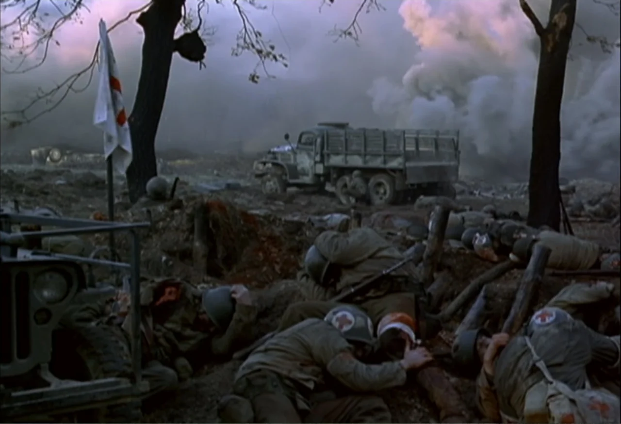 When Trumpets Fade (1998) movie still: wide — A muddy trench occupied by medical soldiers during a conflict. Military personnel lay low in the dirt…