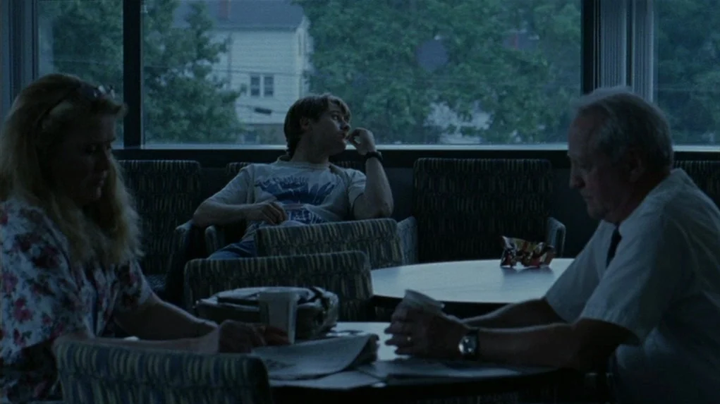 Junebug (2005) movie still: wide — A waiting area with dark patterned upholstery and a large glass window behind.