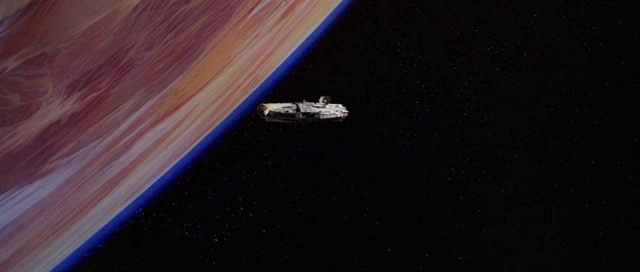 Star Wars (1977) movie still: wide — A detailed model spaceship floats against the vast dark void of deep space. A large planetary surface with…