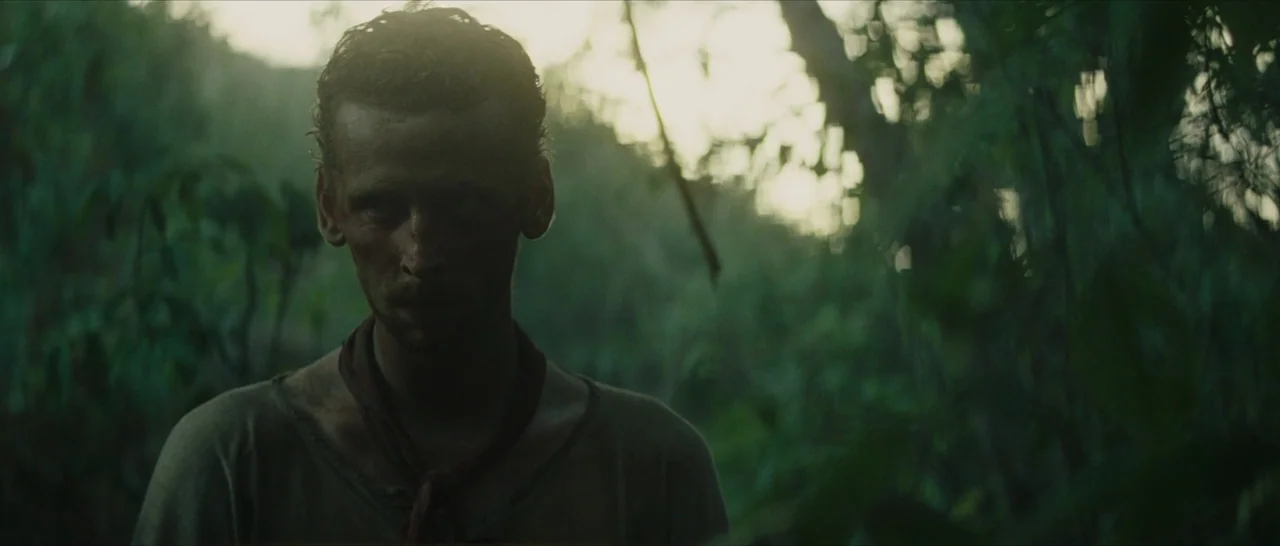 The Lost City of Z (2016) movie still: medium — A man stands in a thick, dimly lit jungle with dense foliage surrounding him. Sunlight filters…
