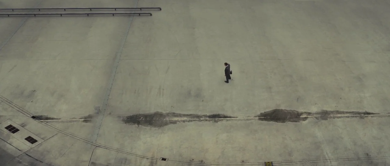 High-Rise (2015) movie still: establishing — An expansive, empty gray concrete area features structural expansion joints and metal railings. A…