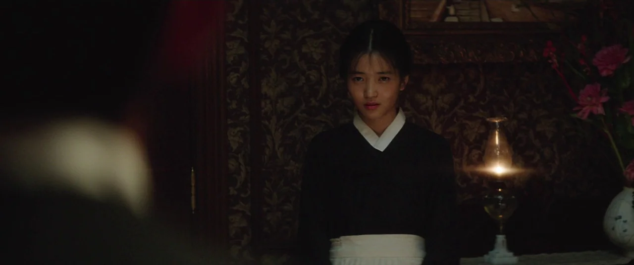 The Handmaiden (2016) movie still: medium — A dimly lit room with ornate, dark floral wallpaper and wood paneling. A young woman in a black and…