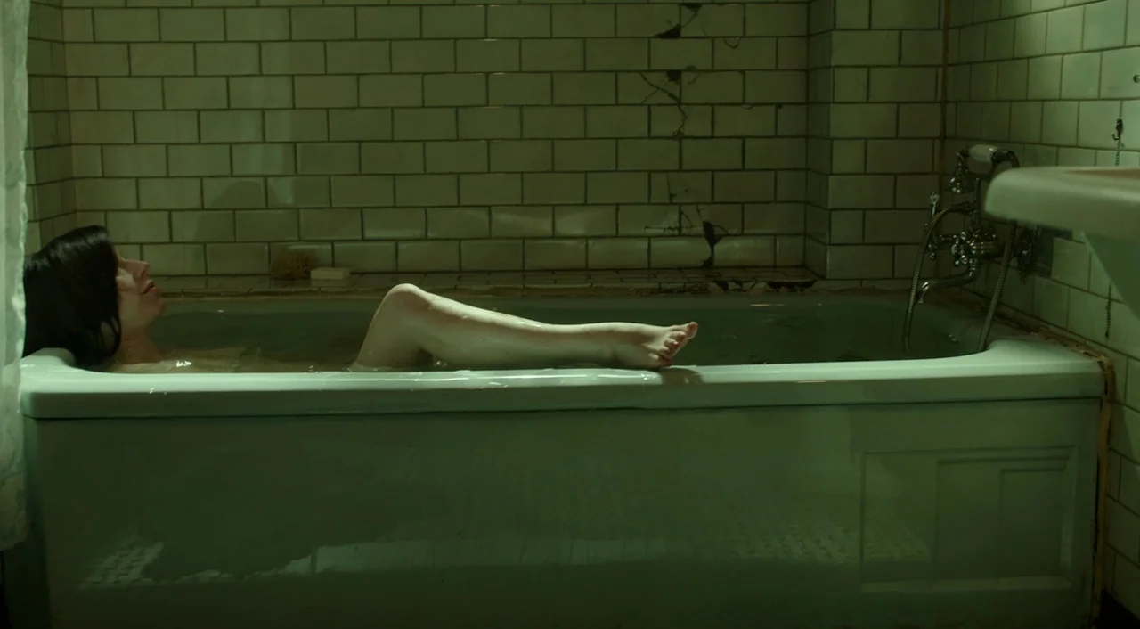 The Shape of Water (2017) movie still: medium — A dimly lit room with green-tinted white subway tiles featuring cracks in the wall. A woman with…