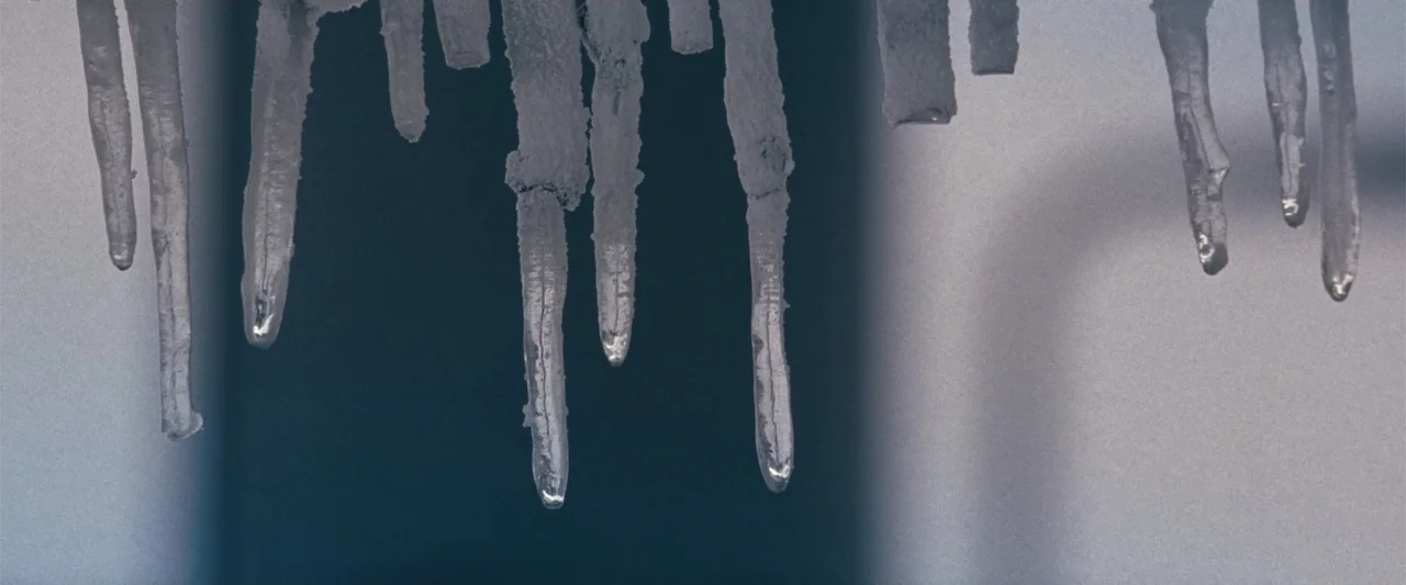 Frozen (2010) movie still: closeup — A row of sharp icicles hangs vertically from the edge of a structure. The background is a soft-focus gradient…