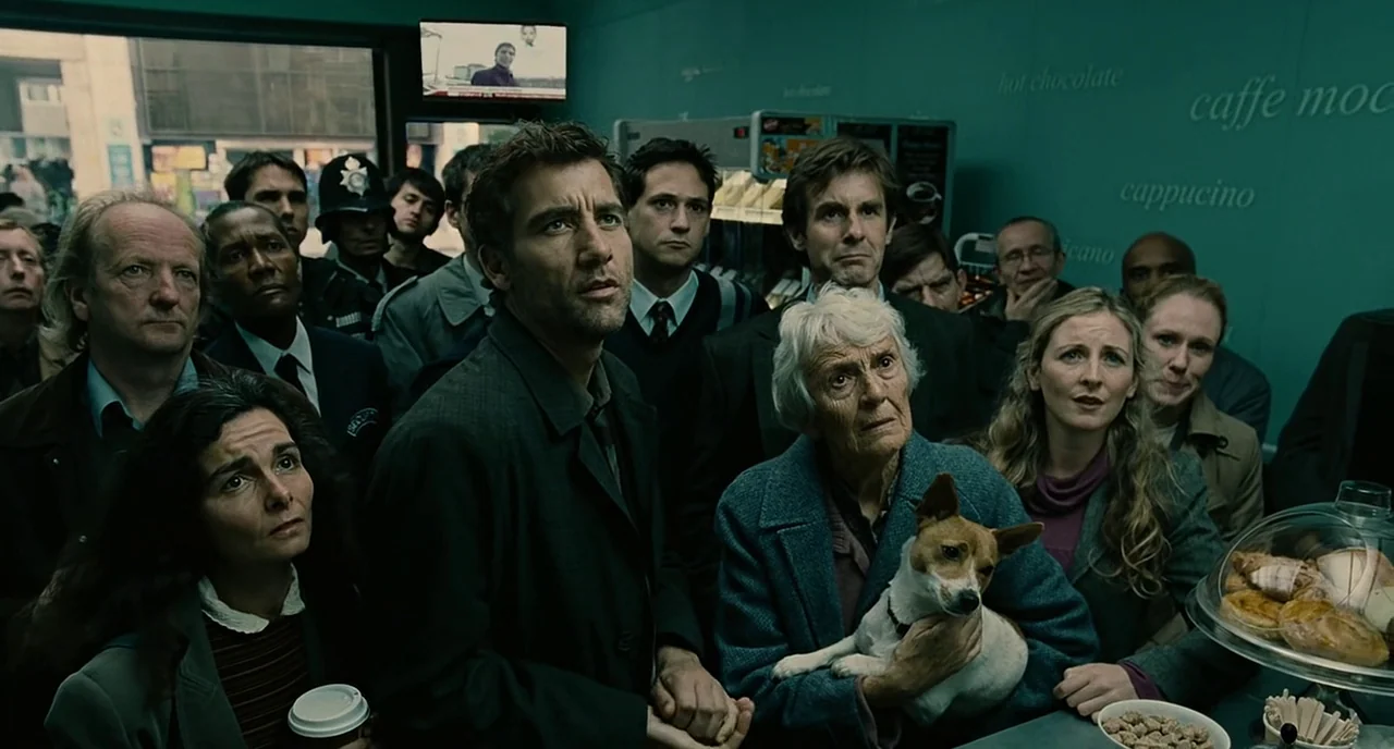 Children Of Men (2006) movie still: medium — A crowded public shop interior features teal walls with white menu text on boards. A diverse group of…