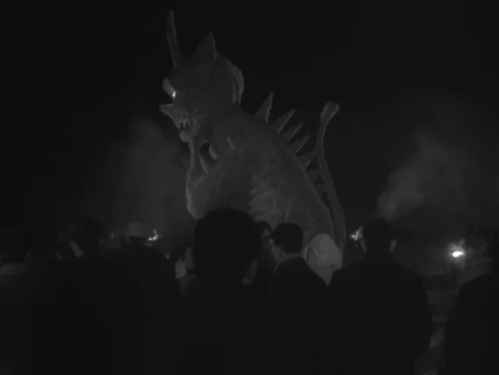 The Idiot (1951) movie still: fullbody — A dark, smoke-filled field at night is occupied by a large group of people. The crowd gathers to observe a…
