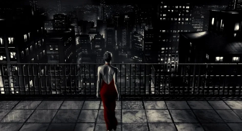 Sin City (2005) movie still: fullbody — A high-rise balcony overlooks a dense cityscape illuminated by glowing windows at night. A woman in a red…