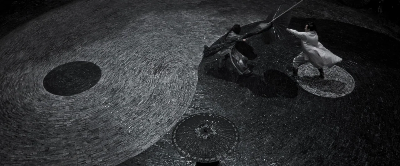Shadow (2018) movie still: wide — A stone courtyard features a large circular yin-yang symbol paved into the ground. Two figures engage in combat…
