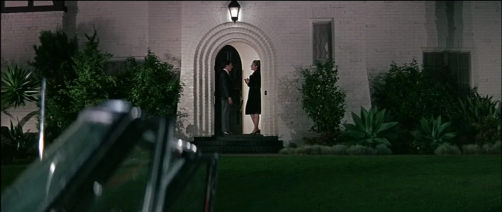 The Graduate (1967) movie still: wide — A white brick house at night features a prominent arched doorway with a light. A man and a woman stand on…