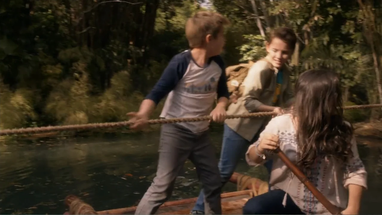 Legends of the Hidden Temple (2016) movie still: medium — A group of children travel on a makeshift wooden raft across a shallow river. The children…