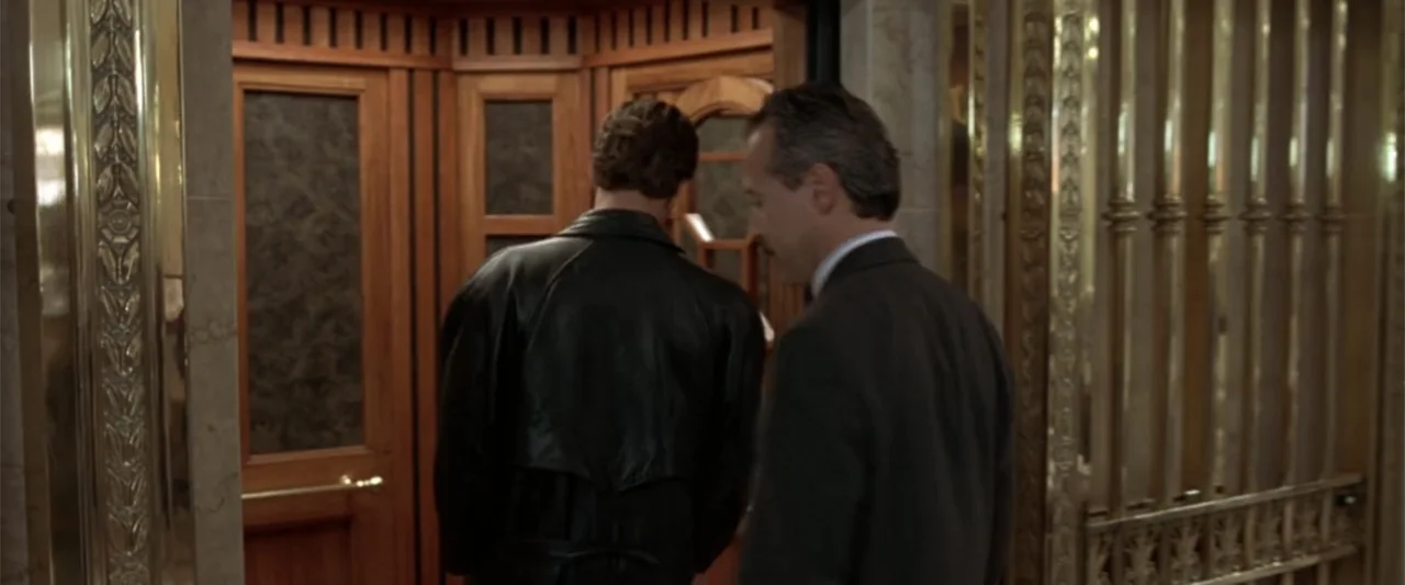 Maximum Risk (1996) movie still: medium — A luxury elevator interior features ornate wood paneling and decorative gold-toned metal grilles. Two men…