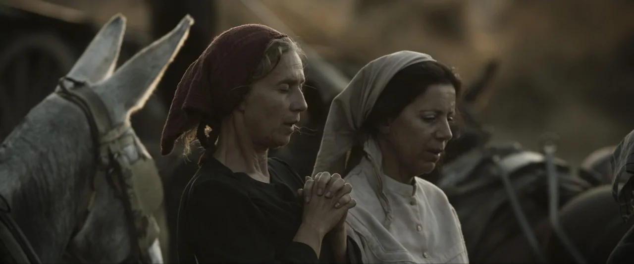 Fatima (2020) movie still: medium — Two women stand outdoors with a donkey visible in the background under soft light. They hold their hands clasped…