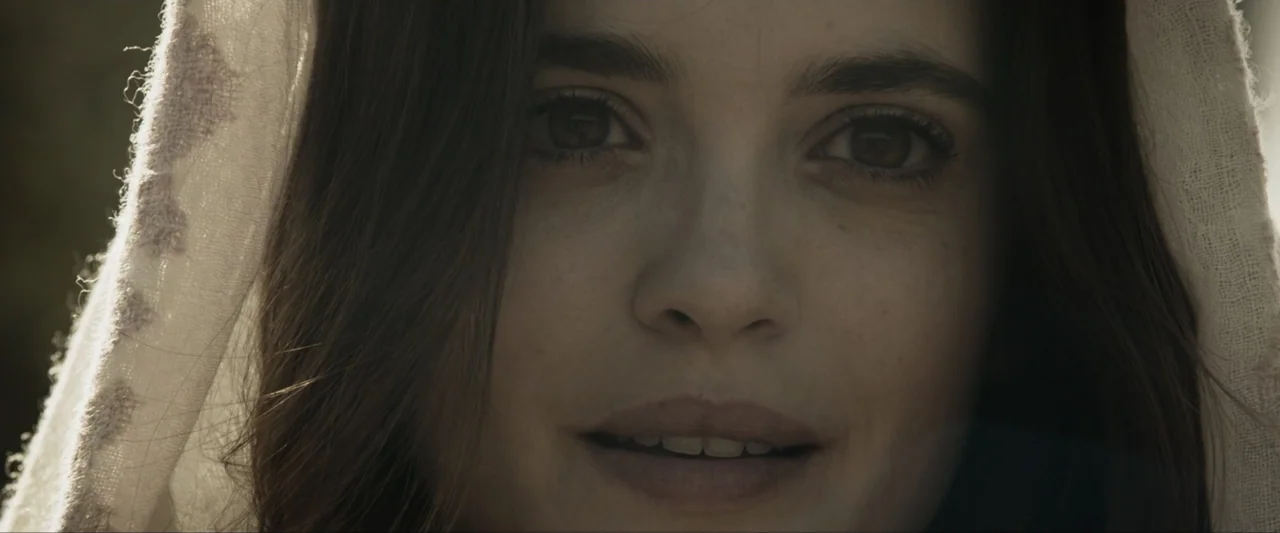 Fatima (2020) movie still: closeup — A close-up view shows a woman standing outdoors during a warm, sunny period. She wears a fabric head covering…