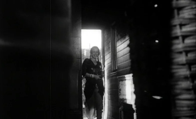 Cairo Station (1958) movie still: medium — A narrow wooden hallway is dark and shadowed with wood paneled walls. A young woman stands in an open…