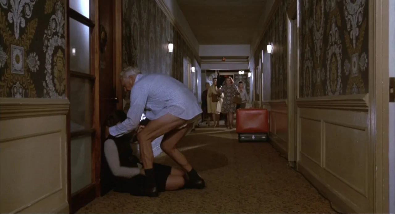 Foxy Brown (1974) movie still: fullbody — A long hotel corridor features ornate patterned wallpaper and beige carpeting with wall sconces. An older…