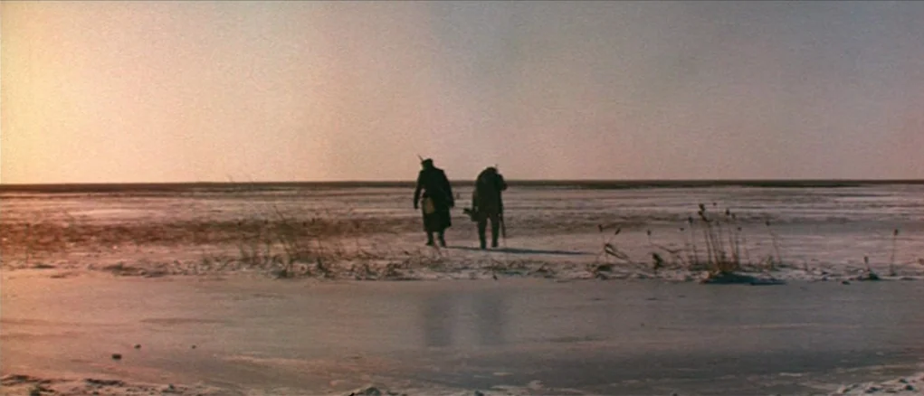 Dersu Uzala (1975) movie still: wide — A vast, flat, and desolate frozen plain extends toward a distant, low horizon line. Two figures in heavy…