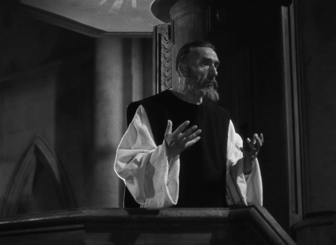 Le Corbeau (1943) movie still: medium — A wooden pulpit situated within a dim stone architectural space with Gothic pointed arches. A bearded man in…