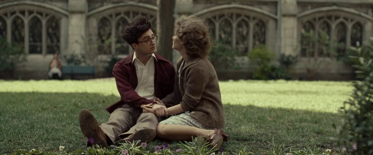 Kill Your Darlings (2013) movie still: fullbody — A quiet grassy courtyard enclosed by gothic stone arches with arched windows. A young couple sits…