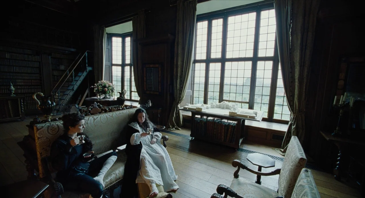 The Favourite (2018) movie still: wide — A spacious library features dark wood paneling, tall windows, and a built-in bookshelf. Two women in…