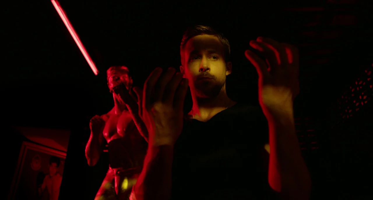 Only God Forgives (2013) movie still: medium — A dark space features red neon accents and a statue of a fighter. A man wearing a black shirt poses…