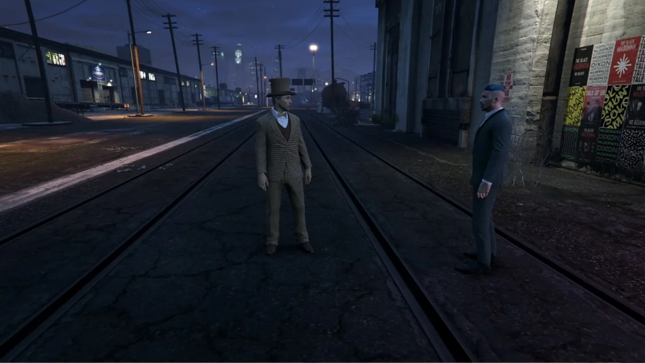 Grand Theft Hamlet (2024) movie still: fullbody — A desolate urban rail corridor at night is flanked by industrial warehouses and posters. Two men…
