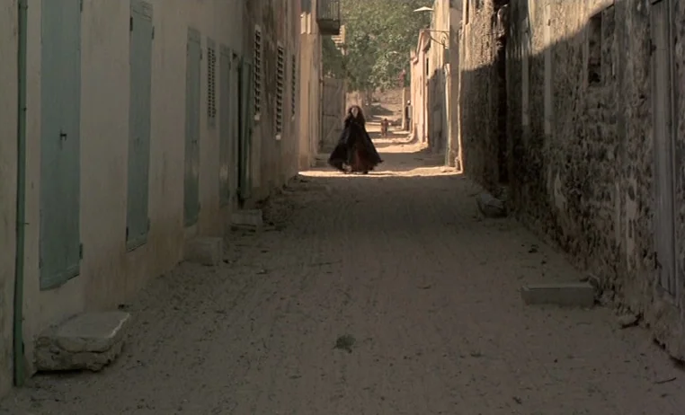 The Story of Adele H (1975) movie still: wide — A narrow sandy path is flanked by high stone walls and green-shuttered buildings. A woman in a dark…