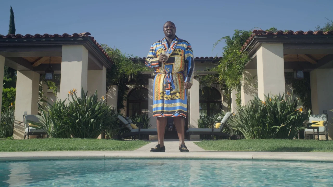 The Laundromat (2019) movie still: fullbody — A man stands on the edge of a swimming pool in front of a villa. The background features open-air…