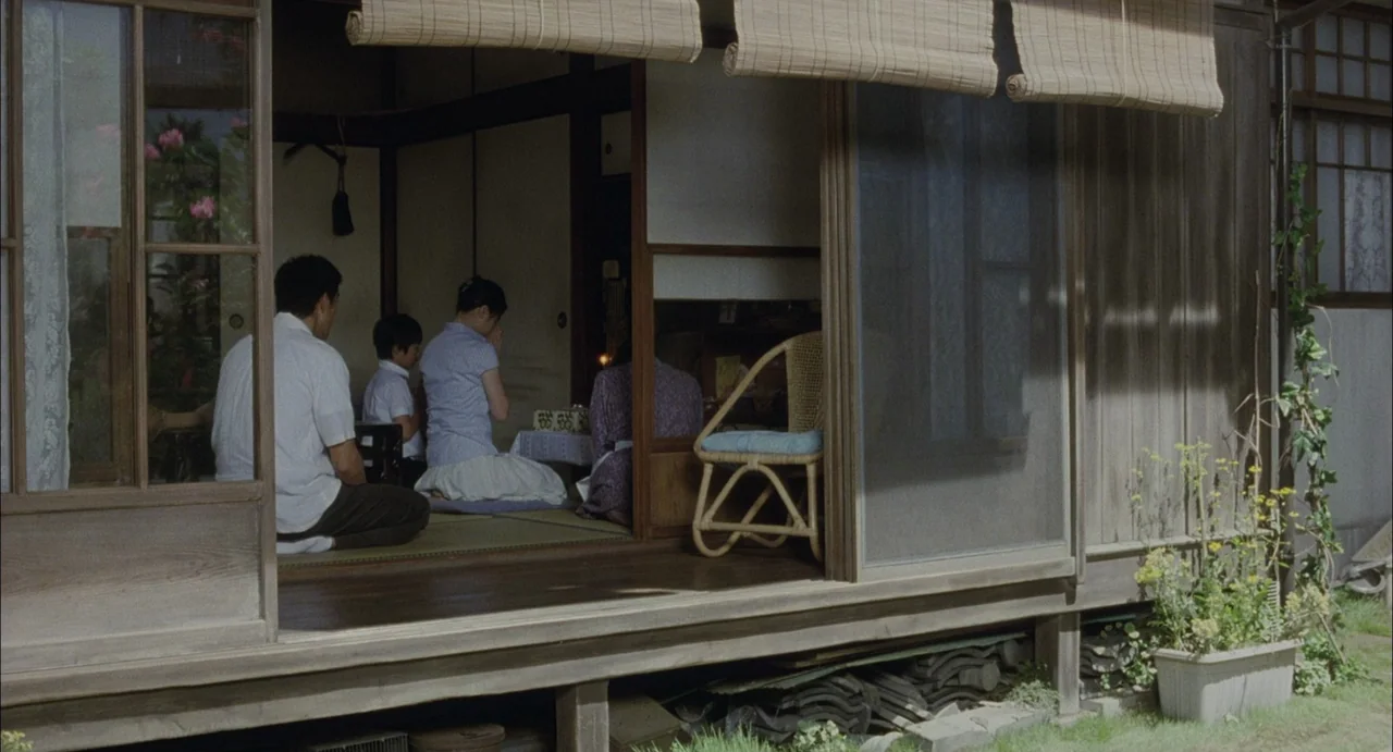 Still Walking (2008) movie still: wide — A traditional Japanese house features a wooden porch and open paper-paned sliding doors. A family of three…