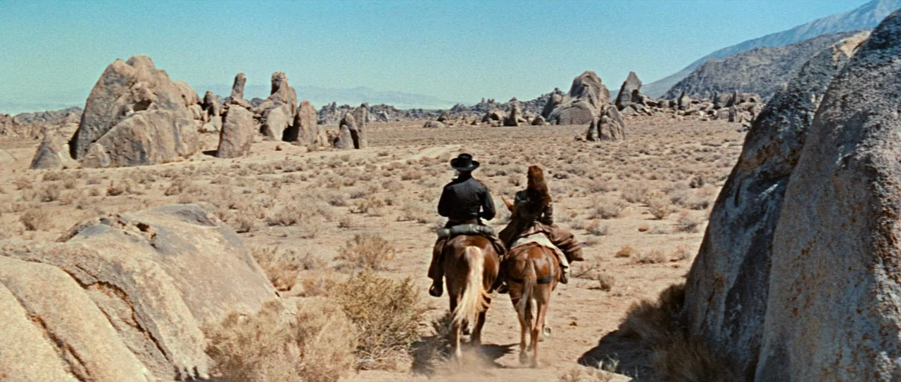 Comanche Station (1960) movie still: wide — An arid rocky desert basin with sparse scrub brush and large granite boulders. A man and a woman on…