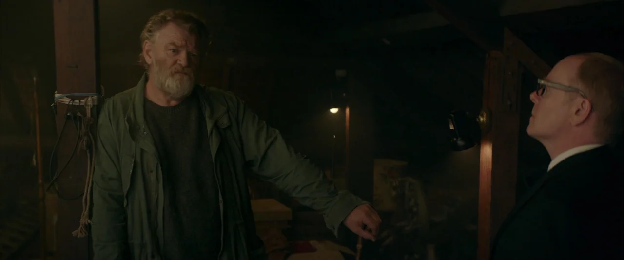 Hampstead (2017) movie still: medium — A dimly lit attic with wooden rafters and shadows obscuring the background. An older bearded man in a jacket…