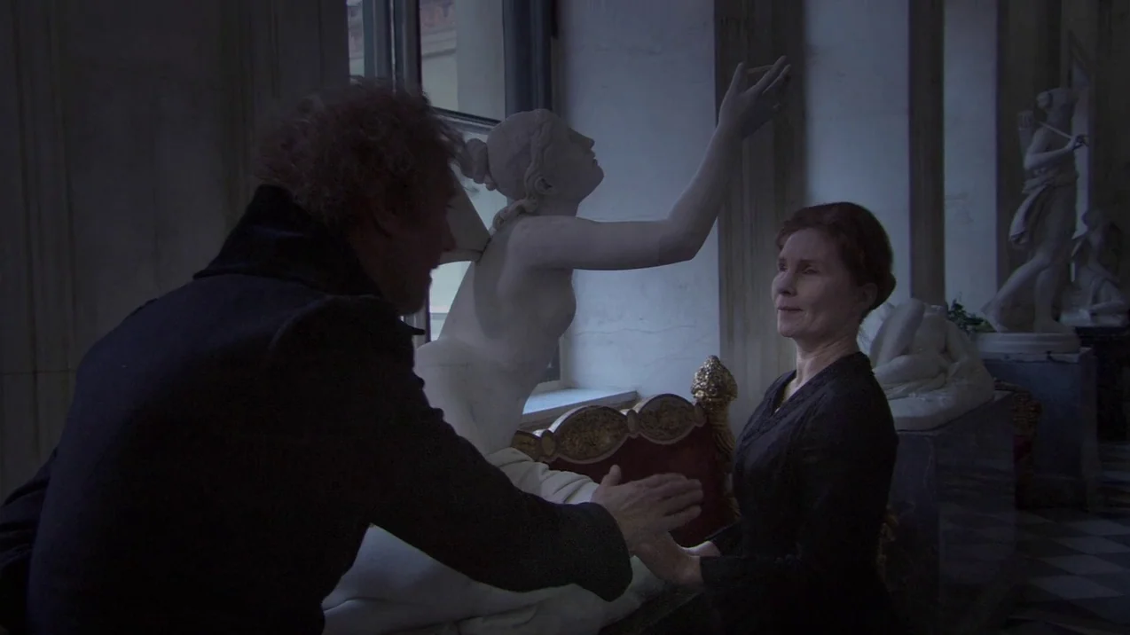 Russian Ark (2002) movie still: medium — A quiet museum hallway features marble sculptures under natural light from large windows. An older man and…