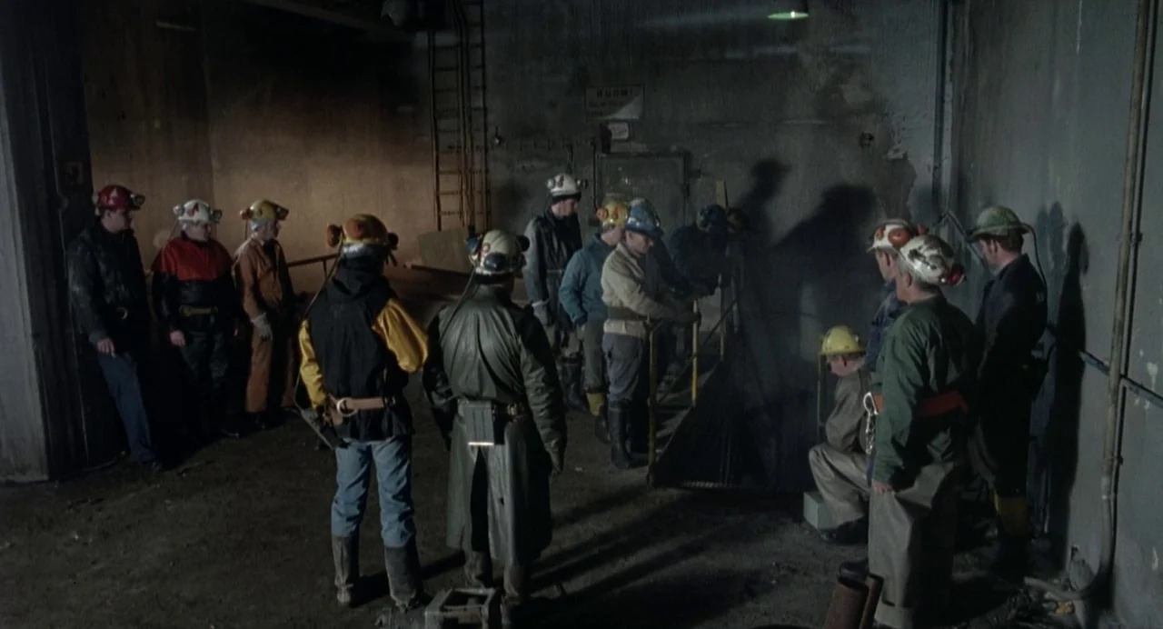 Ariel (1988) movie still: wide — A dimly lit industrial space with concrete walls and exposed wiring. Several men in protective gear and mining…
