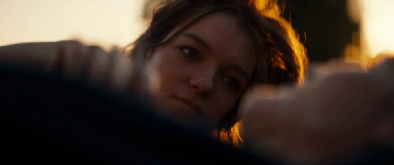 Silver Haze (2023) movie still: closeup — An open field is illuminated by the low angle of a setting sun. A young woman lies in the grass, resting…