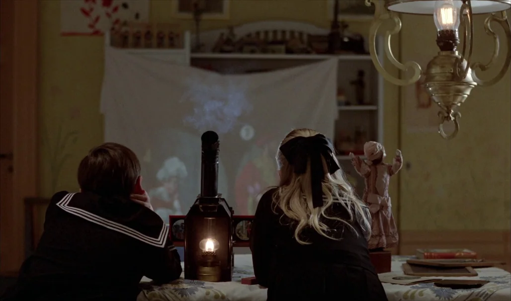 Fanny and Alexander (1982) movie still: medium — A dimly lit room features a screen draped over a white shelf for projections. Two children in…